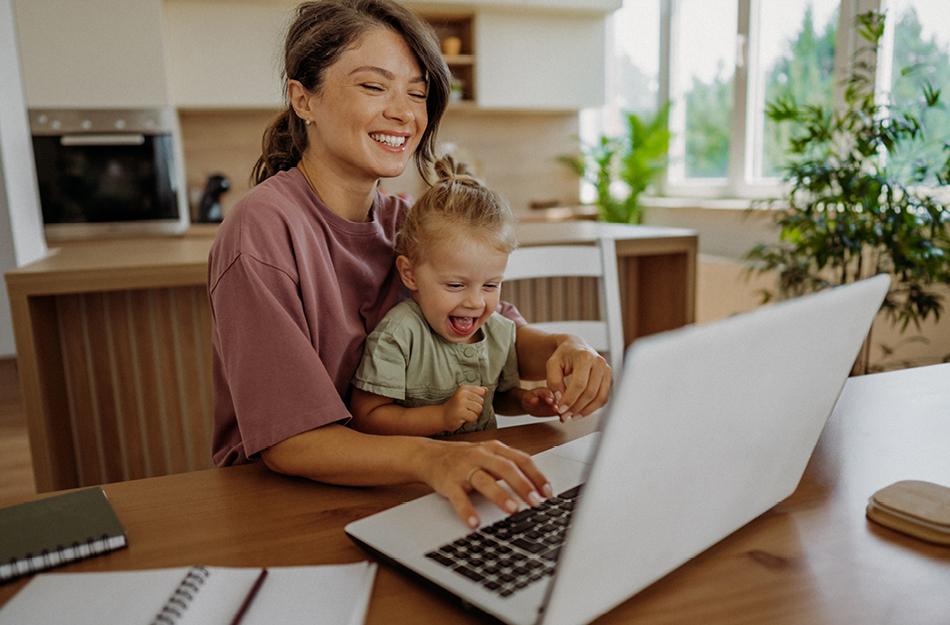 woman working on her computer while holding a baby