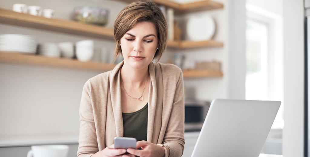 A woman looking at her phone and computer. 